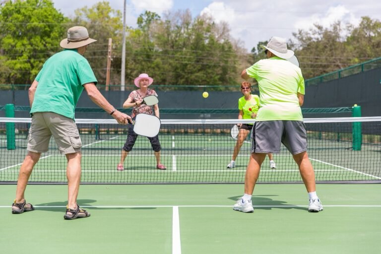 four players in sun hats trading shots at the net on an outdoor pickleball court