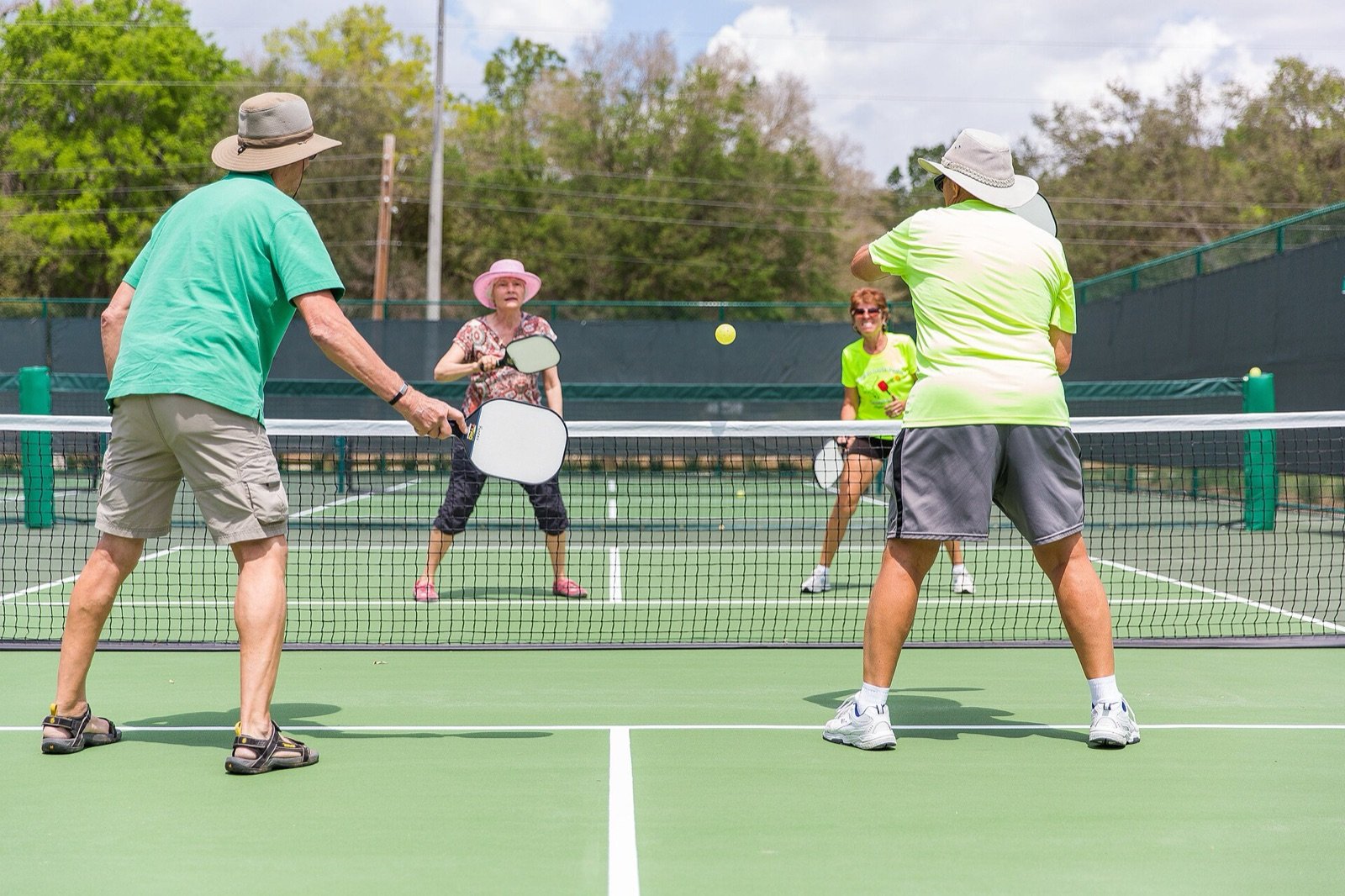 four players in sun hats trading shots at the net on an outdoor pickleball court