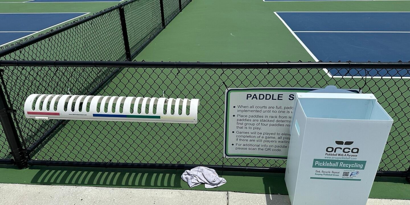 pickleball paddles stacked on a courtside rack while players wait for the next game
