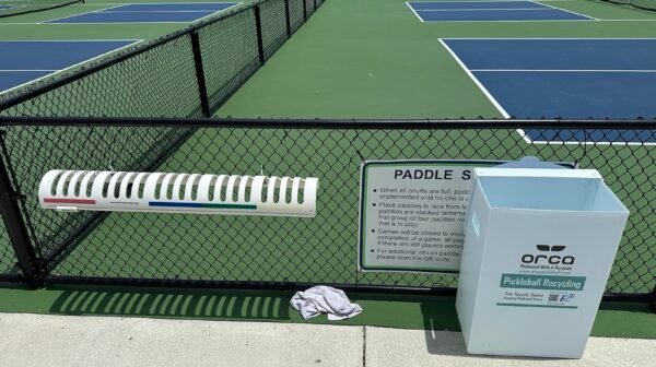 pickleball paddles stacked on a courtside rack while players wait for the next game