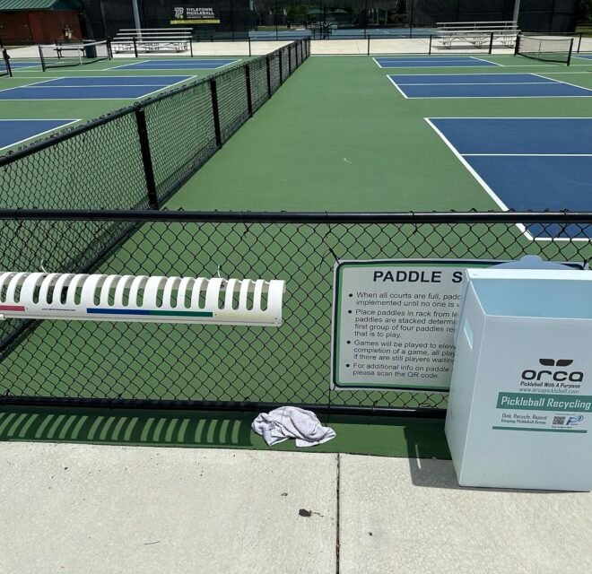 pickleball paddles stacked on a courtside rack while players wait for the next game