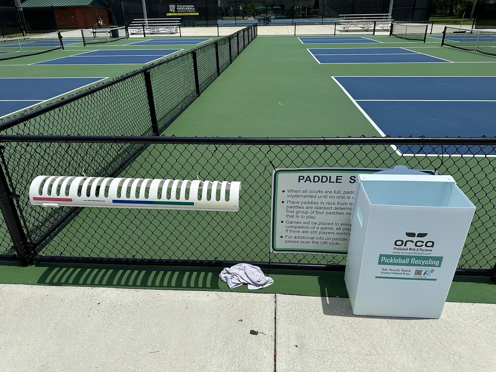 pickleball paddles stacked on a courtside rack while players wait for the next game