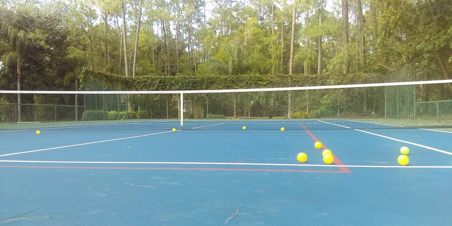 pickleballs and gear resting on the baseline of an outdoor pickleball court