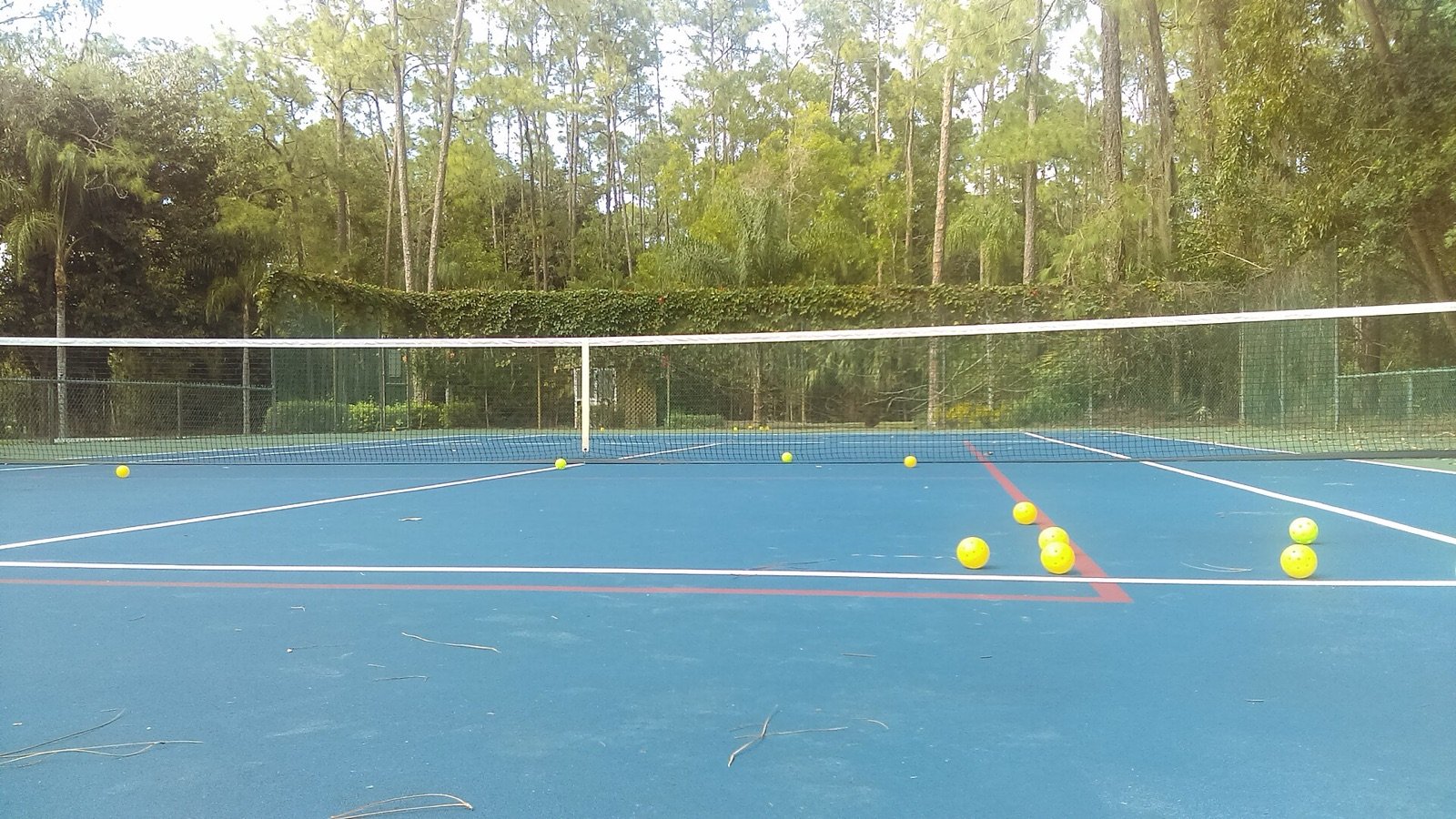 pickleballs and gear resting on the baseline of an outdoor pickleball court